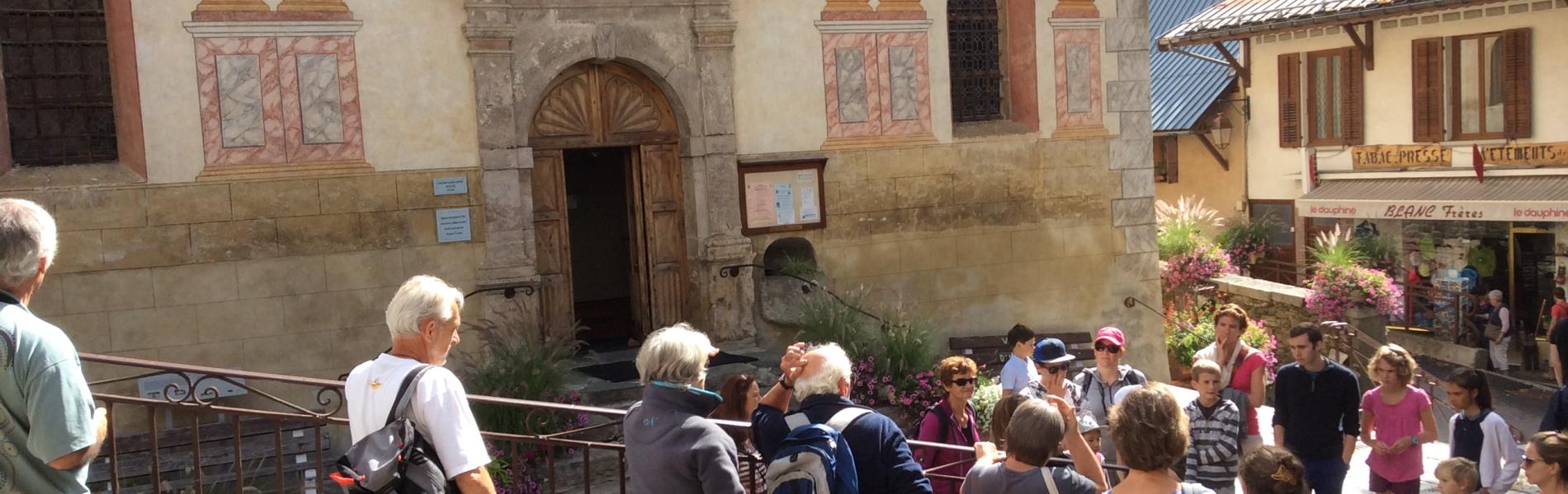 Hauteluce, l'été. Un groupe de personnes devant l'église et ses fresques extérieures