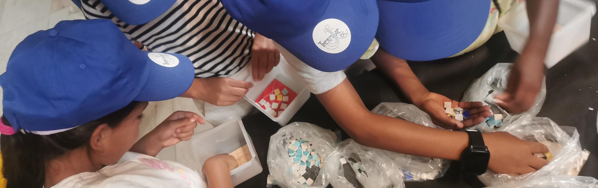 Gros plan sur les mains d'un groupe d'enfants au cours d'un atelier de mosaïque_CMP 2025, Fondation Facim