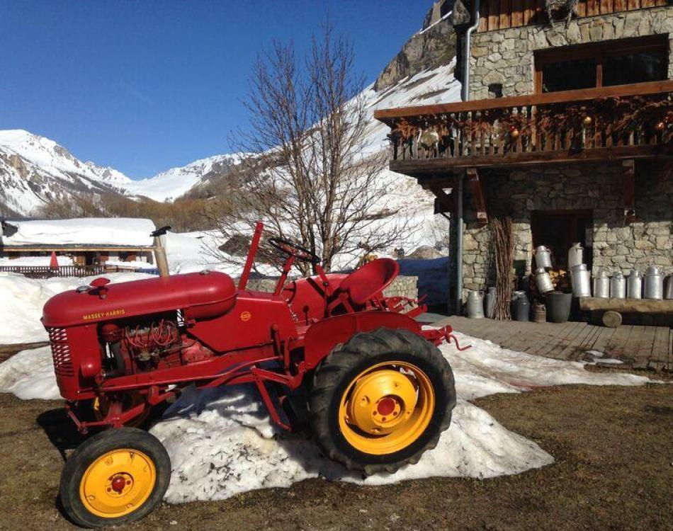 Un tracteur rouge vif sur le blanc de la neige devant une ferme à Val d'Isère