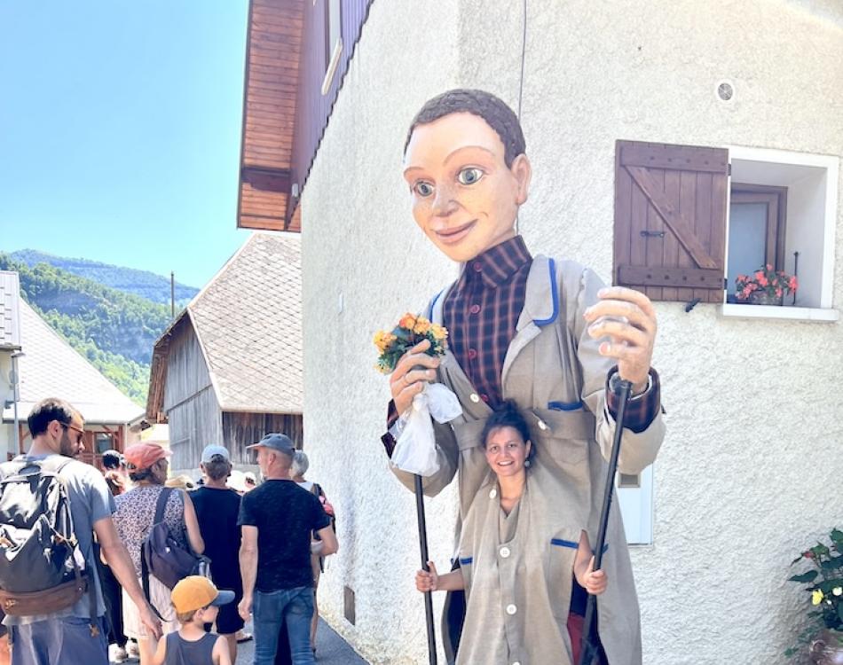 Une marionnette géante dans un village, animée par une artiste souriante