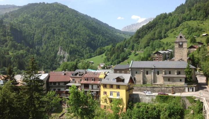 Le village de Flumet - Vue du village de Flumet, son église, ses maisons suspendues depuis la route de la Germandière. Massifs verdoyants en fond.