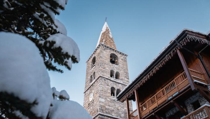 Clocher - Val d'Isère - Vue en contre plongée de l'historique clocher de Val d'Isère avec à sa gauche un bout de sapin et un chalet typique à droite.