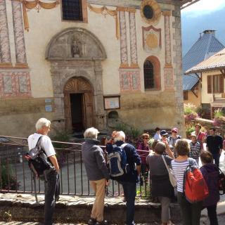 Hauteluce, l'été. Un groupe de personnes devant l'église et ses fresques extérieures