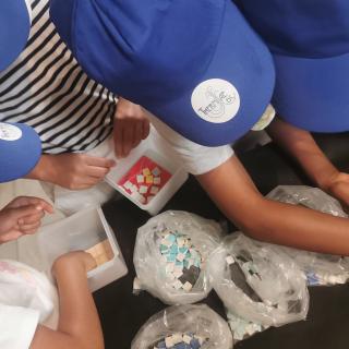 Gros plan sur les mains d'un groupe d'enfants au cours d'un atelier de mosaïque_CMP 2025, Fondation Facim
